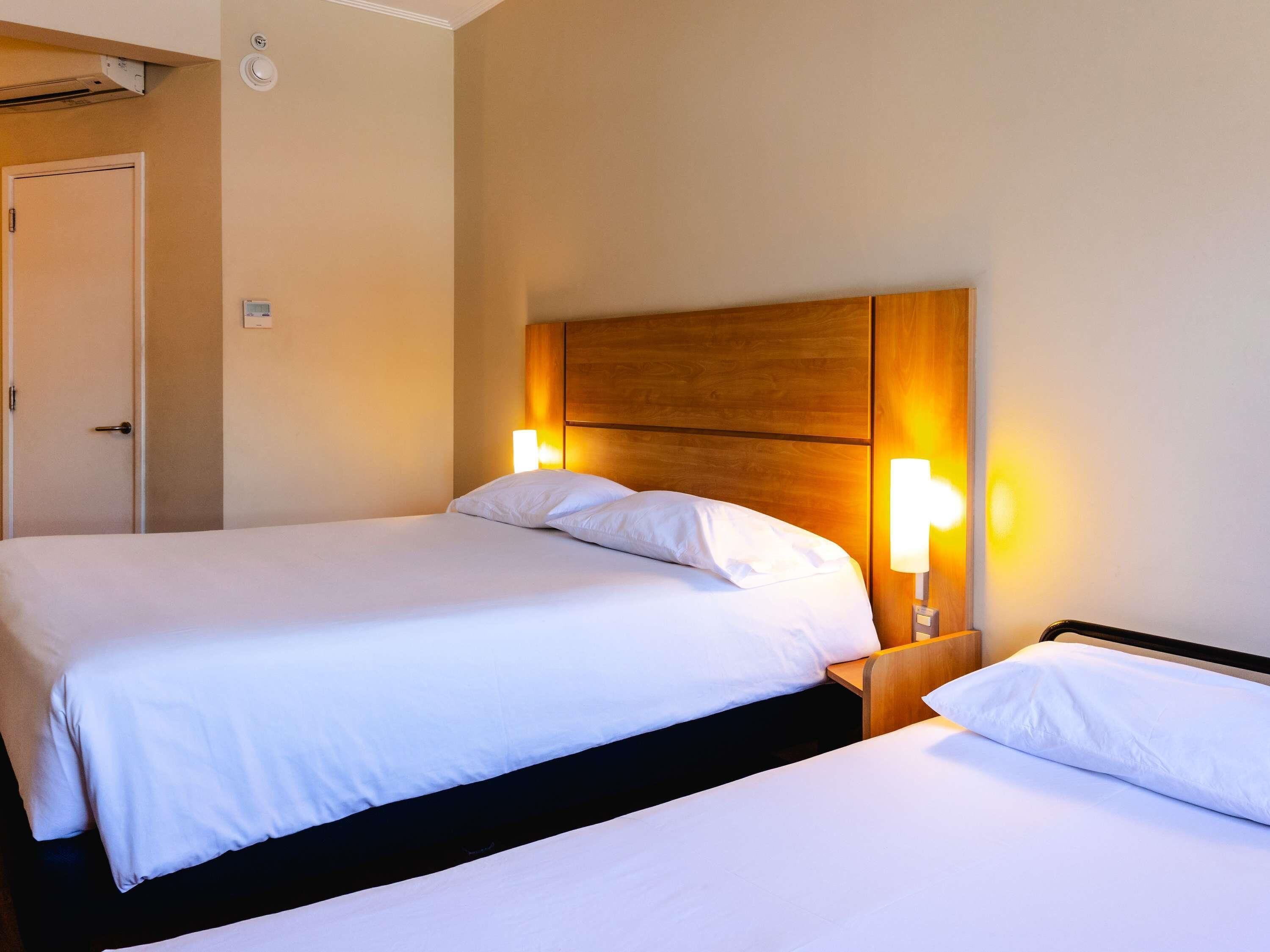 A hotel room with two beds, a wooden headboard, bedside lamps, and a door.