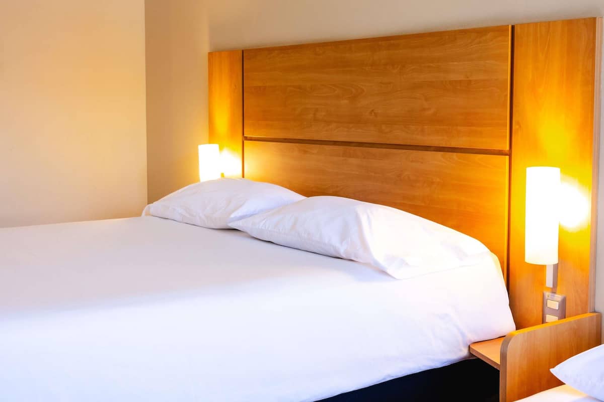 A hotel room with a large bed, wooden headboard, and bedside lamps.