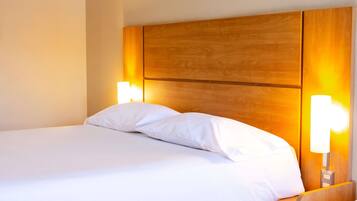 A hotel room with a large bed, wooden headboard, and bedside lamps.