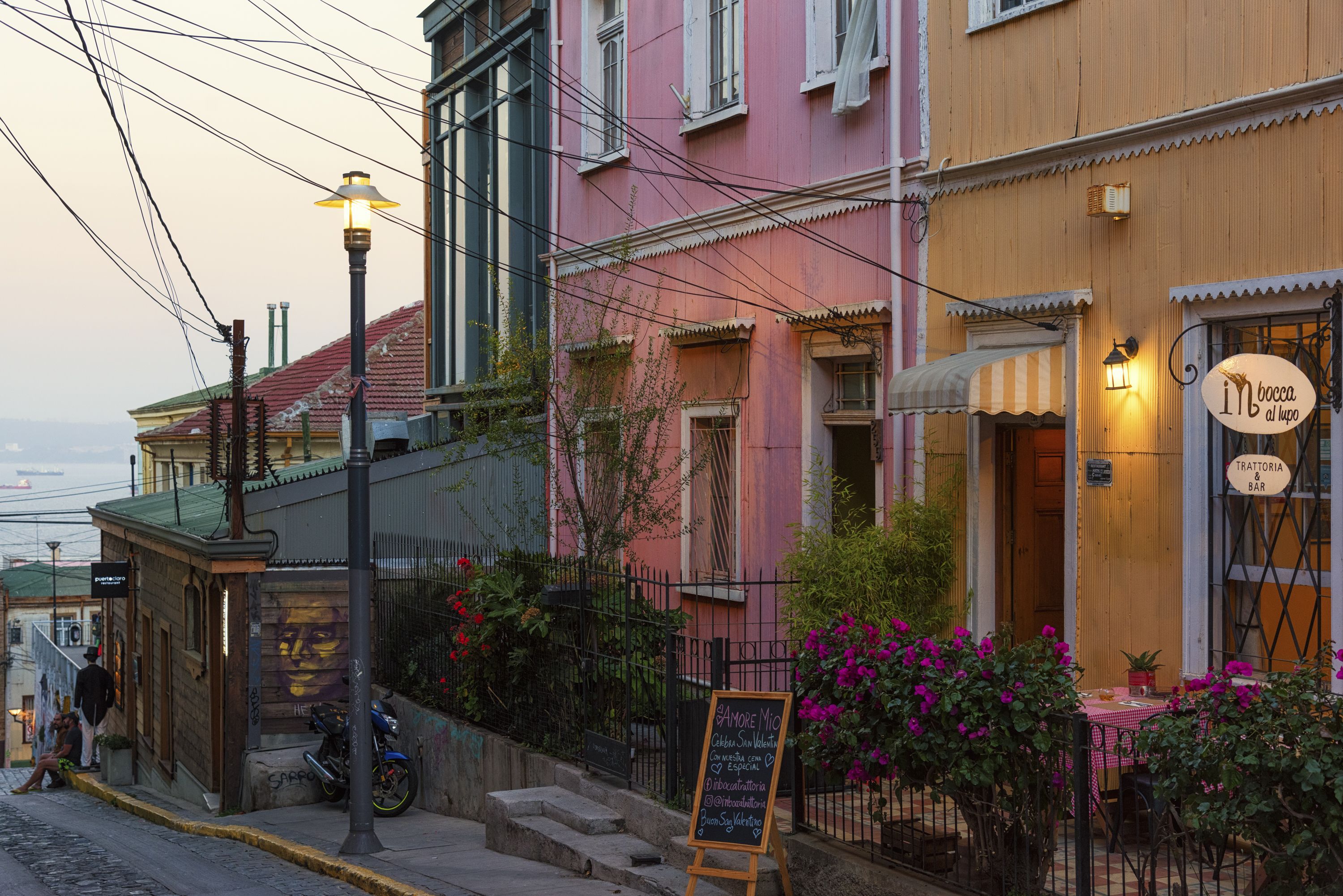 Vista de la calle con un edificio que tiene un restaurante, un menú en pizarra y un pequeño espacio al aire libre con flores.
