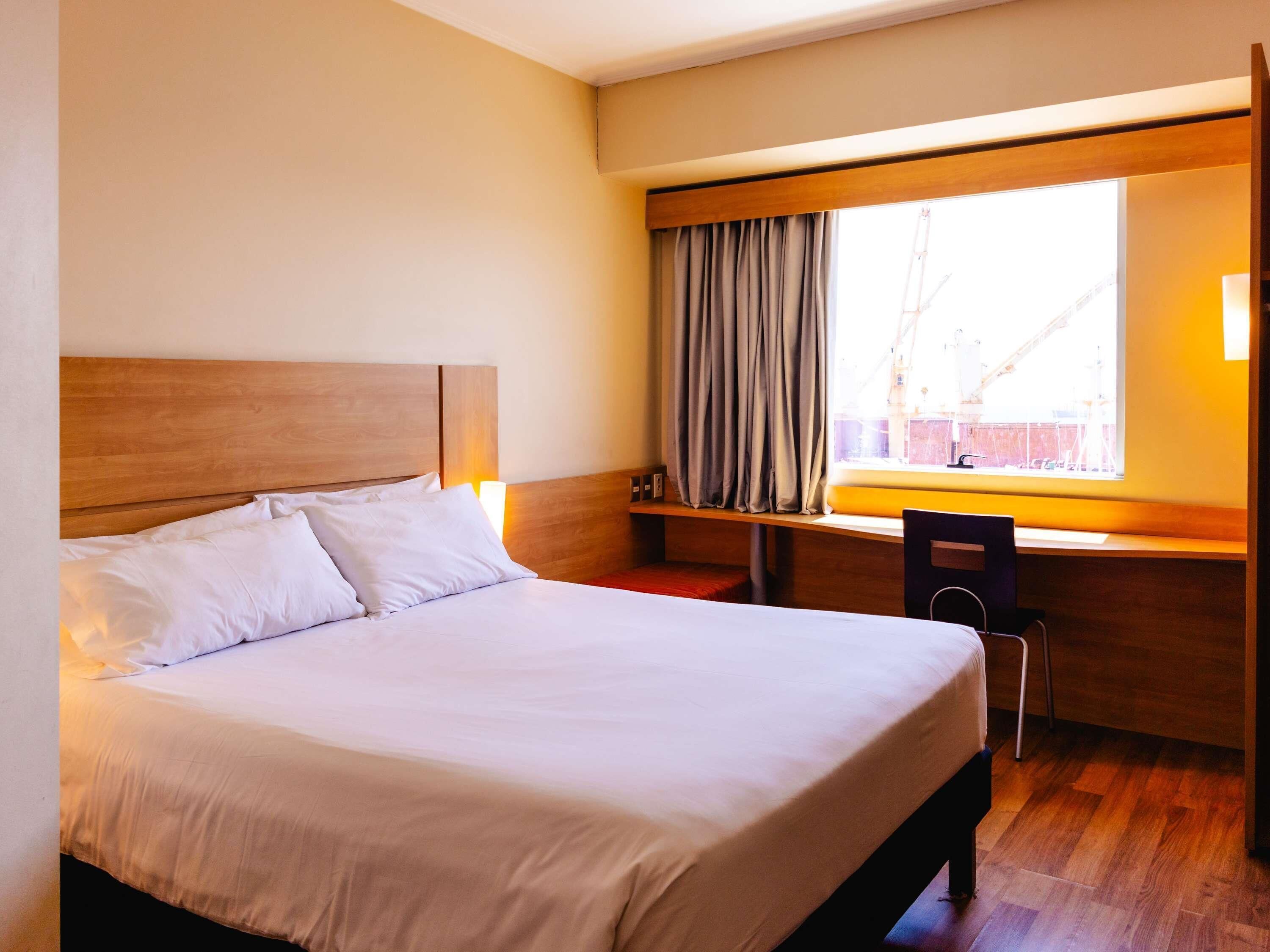 Habitación de hotel con una cama grande, un escritorio con silla y una ventana con cortinas.