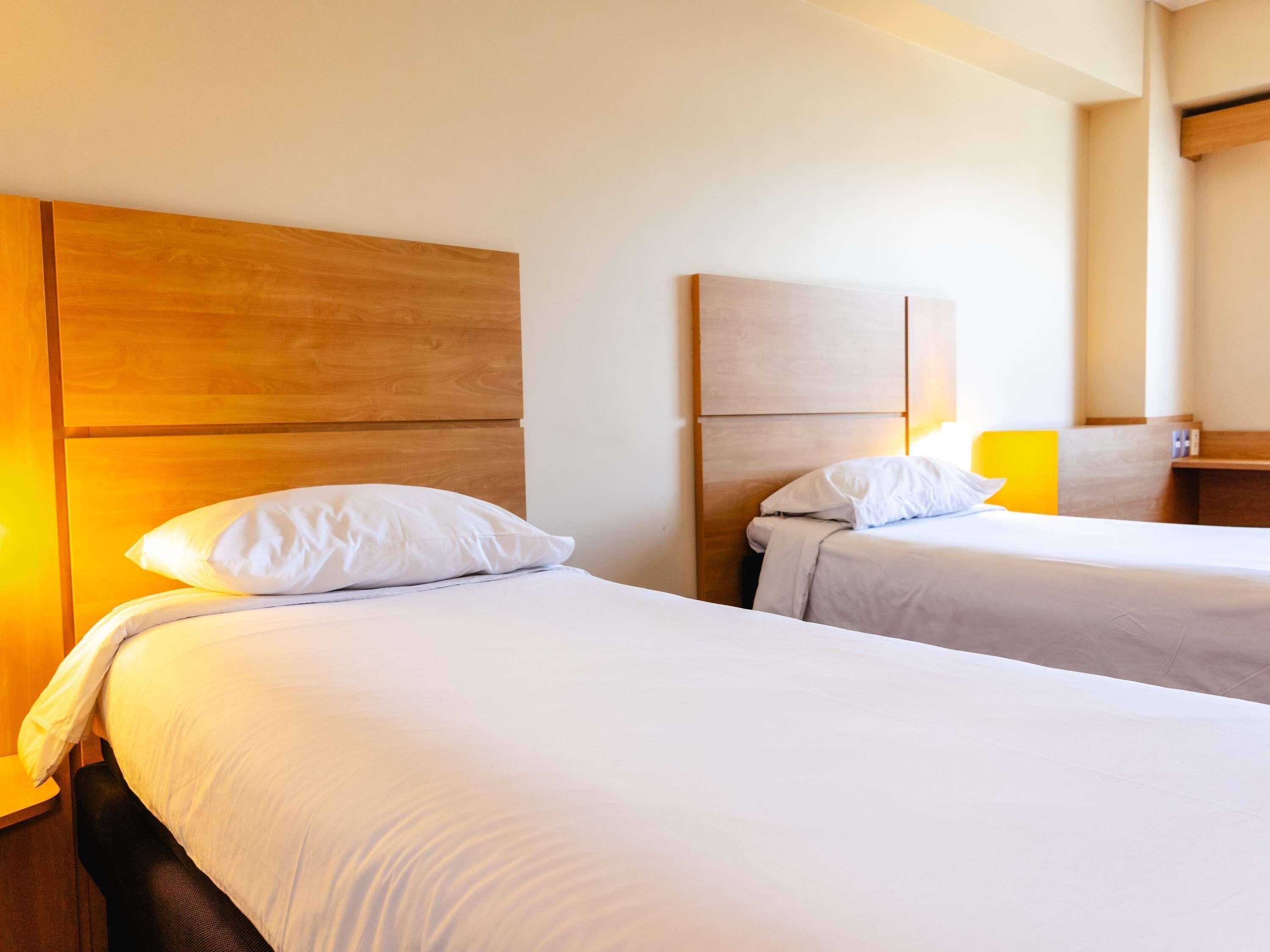 Two single beds with wooden headboards, white bedding, and a bedside table with a lamp.