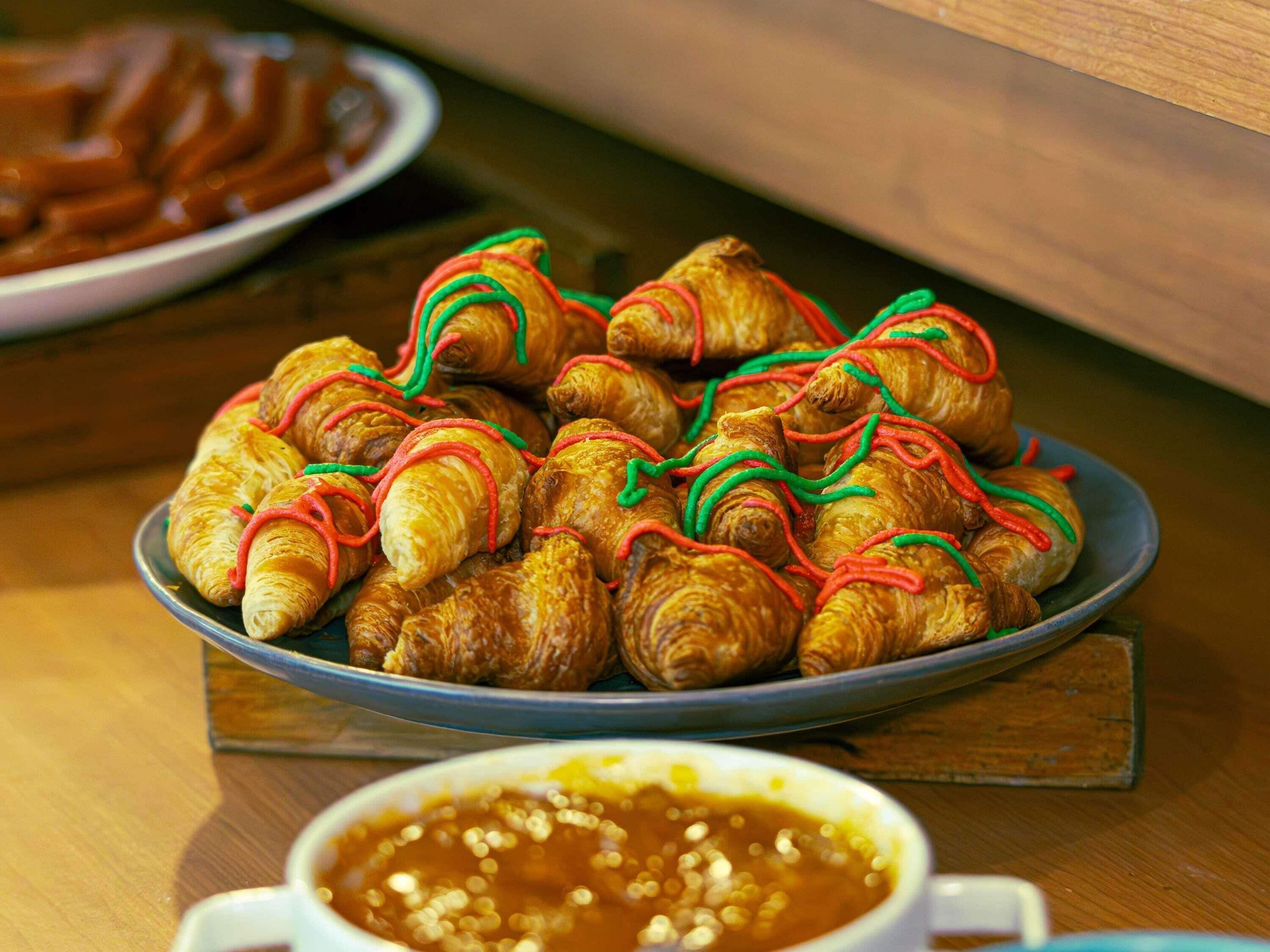 Um prato de croissants com cobertura colorida, uma tigela de molho e uma mesa de madeira.