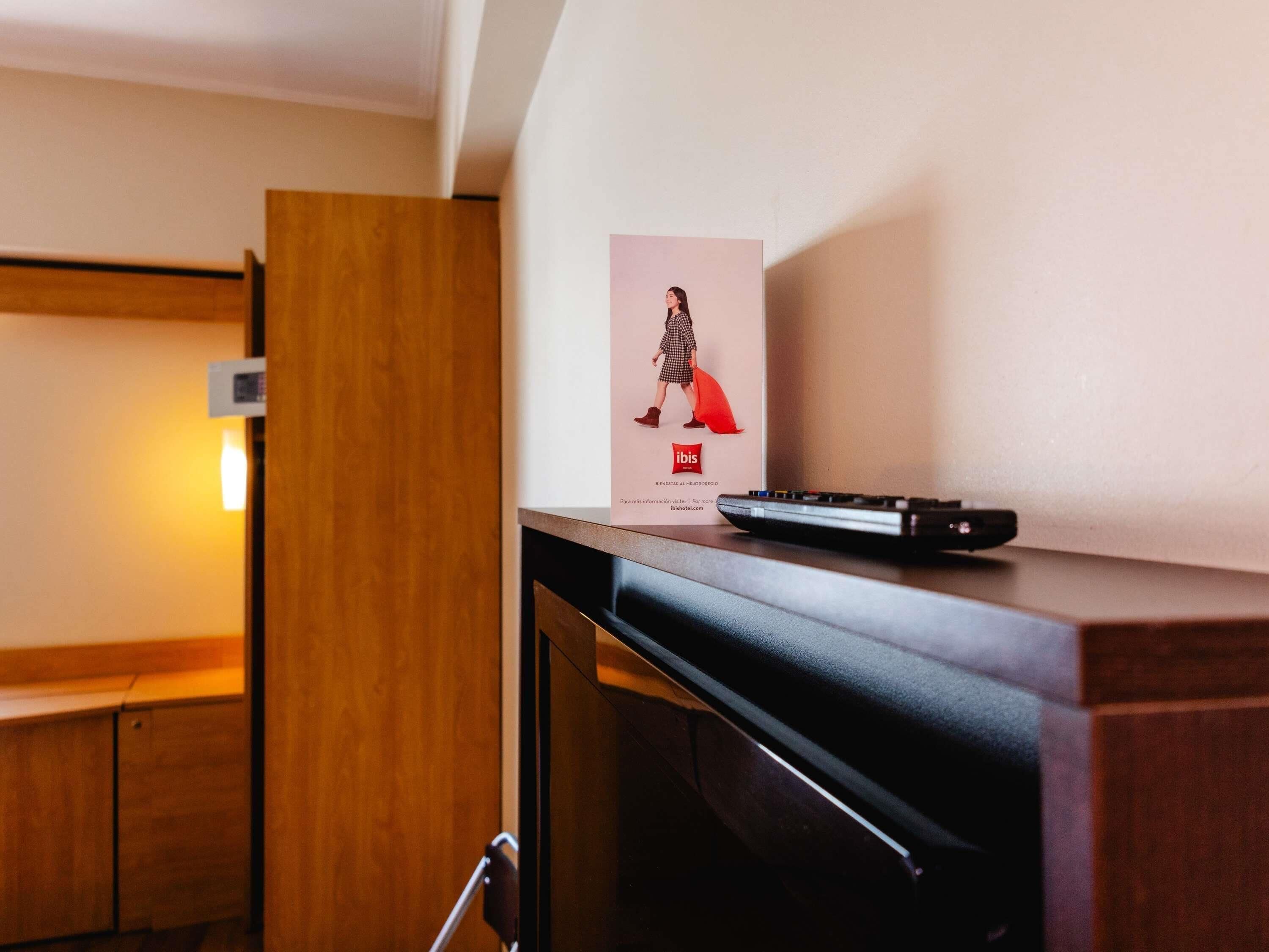 Una habitación de hotel con un armario de madera, un control remoto sobre una encimera y un cartel en la pared.