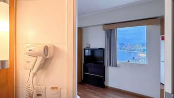 Quarto de hotel com secador de cabelo, televisão, janela com vista para a cidade e piso de madeira.