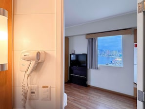 A hotel room with a hairdryer, a TV, a window with a city view, and a wooden floor. - Ibis Valparaiso (Valparaiso)