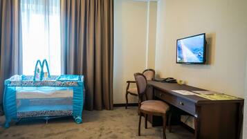 A hotel room with a bed, a desk, a chair, and a television on the wall.