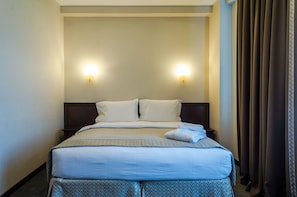 Une chambre d’hôtel avec un lit, deux lampes fixées au mur et un rideau.