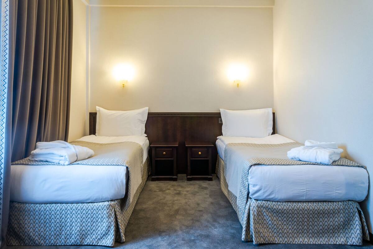 Een hotelkamer met twee eenpersoonsbedden, elk met een bijpassend nachtkastje en een lamp.