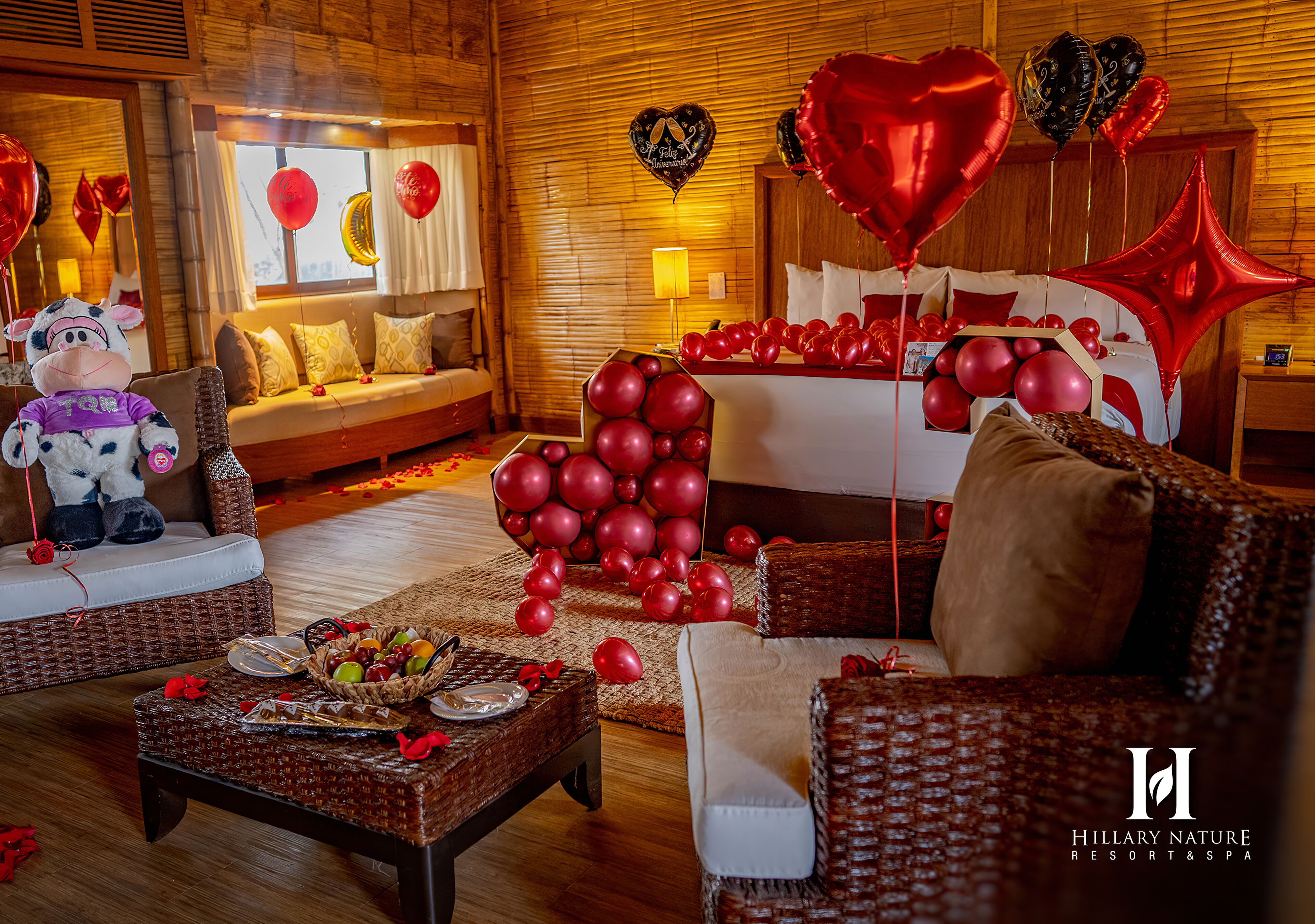 Una habitación acogedora con sofá, una mesa de comedor con una cesta de fruta y una cama con globos rojos.