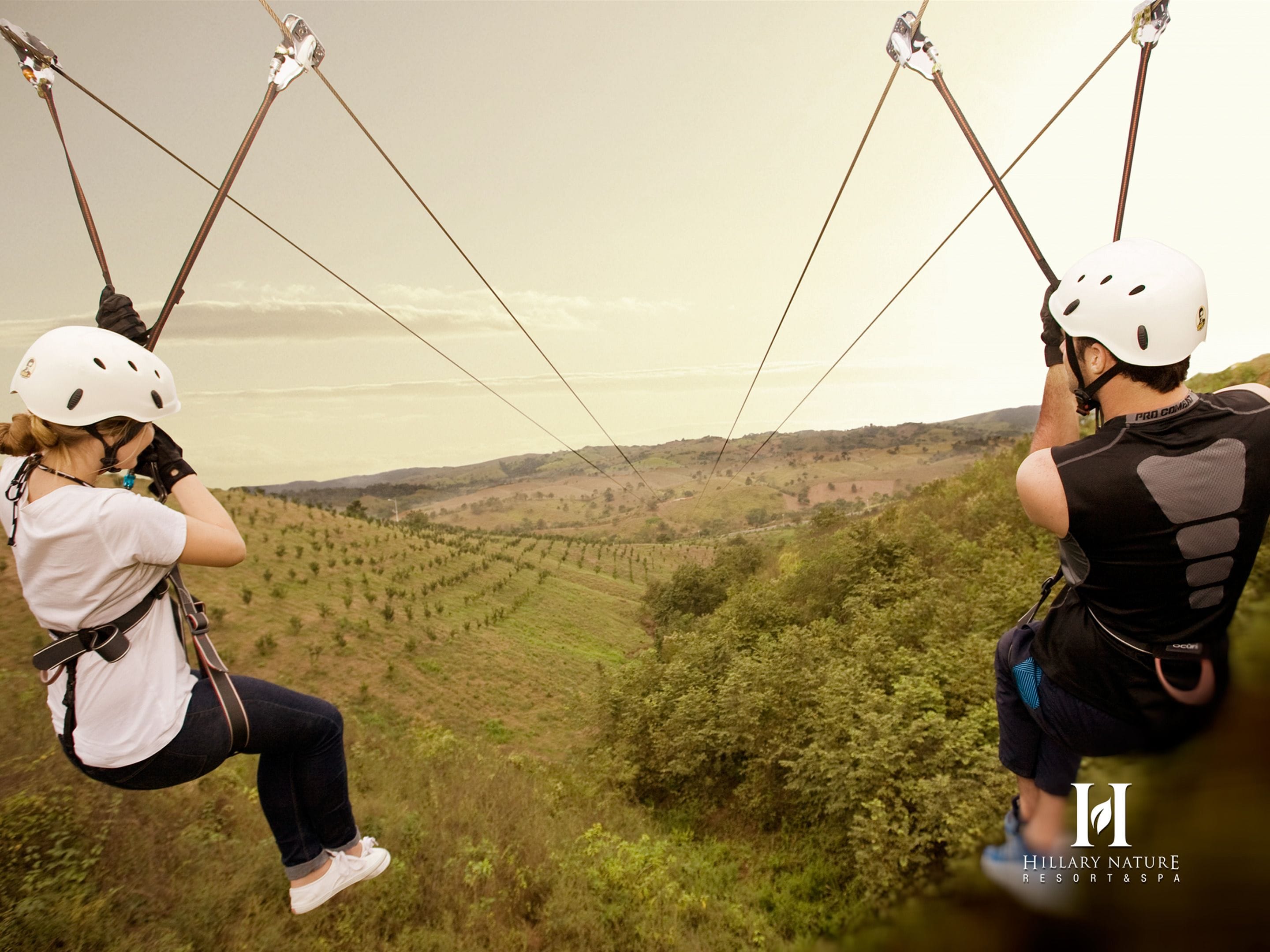 Dos personas en un tirolesa con un paisaje pintoresco al fondo.