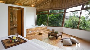 A modern room with a large window, wooden flooring, a bed with a tray of fruit and a glass of juice, and a small seating area with cushions. - Hillary Nature Resort Spa (Arenillas)