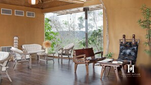 A spacious room with a high ceiling, bamboo beams, wicker furniture, and a view of greenery outside. - Hillary Nature Resort Spa (Arenillas)