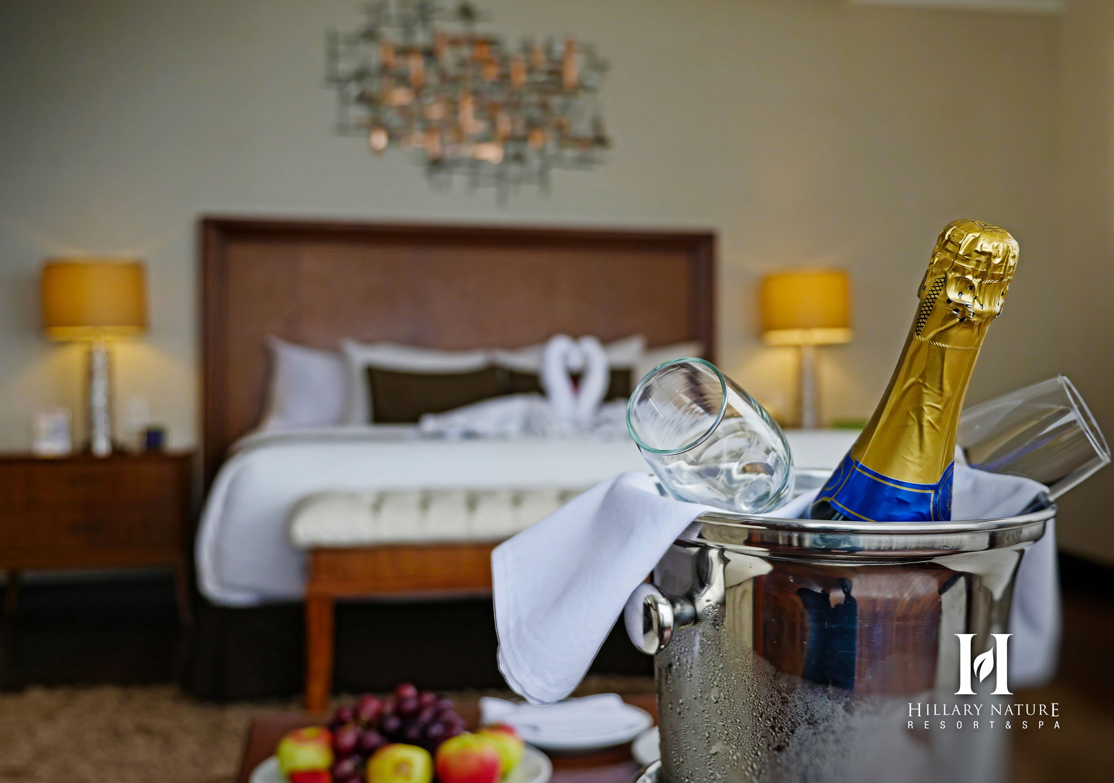 Een hotelkamer met een bed, bedlampen, een minibar en een schaal fruit.