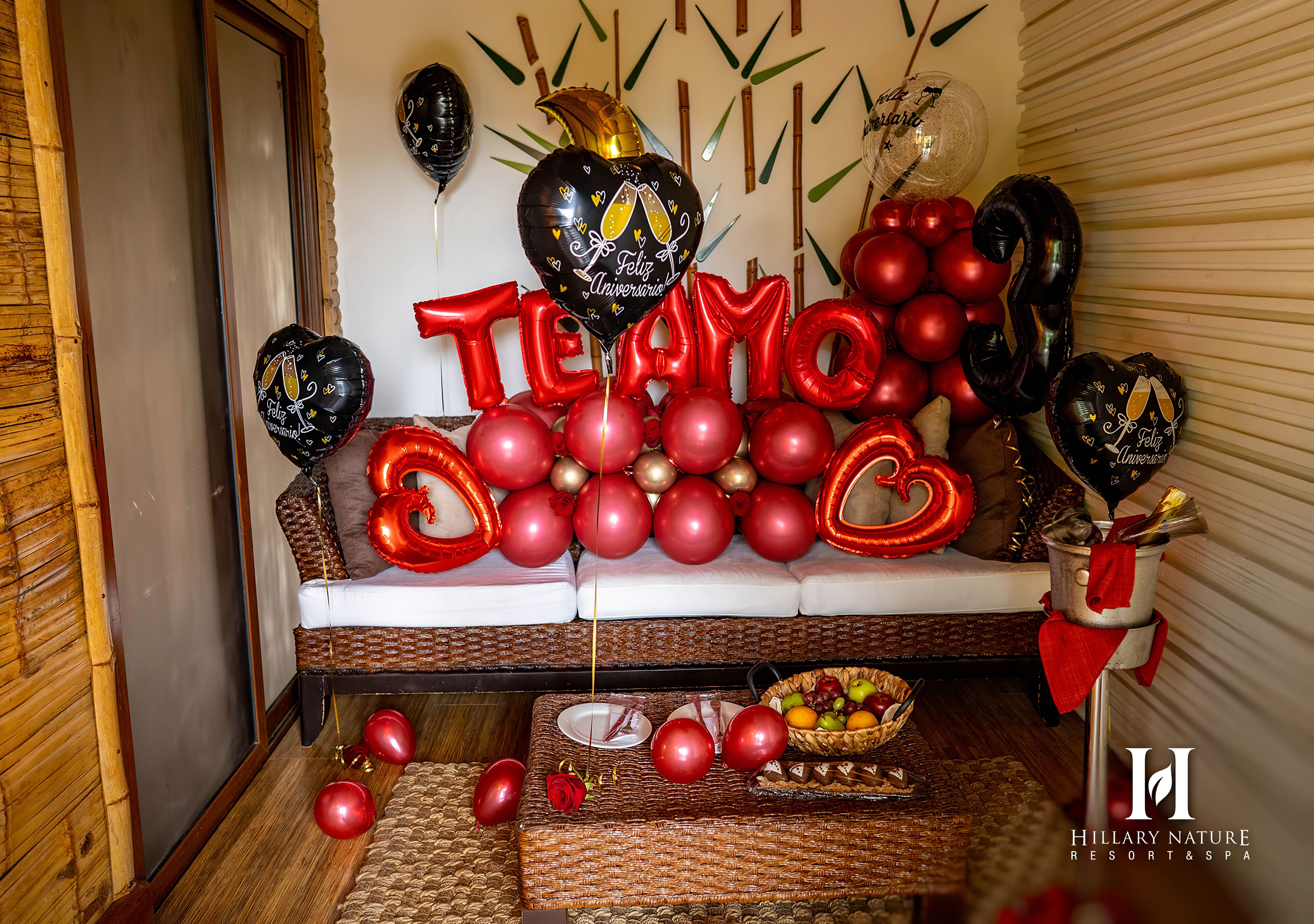 Una habitación con un sofá decorado con globos rojos y negros, una cesta de fruta y una pequeña mesa con un plato y una vela.