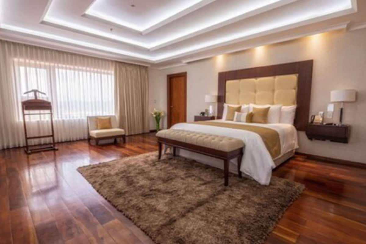 A spacious bedroom with a large bed, a bench, a bedside table, and a nightstand.