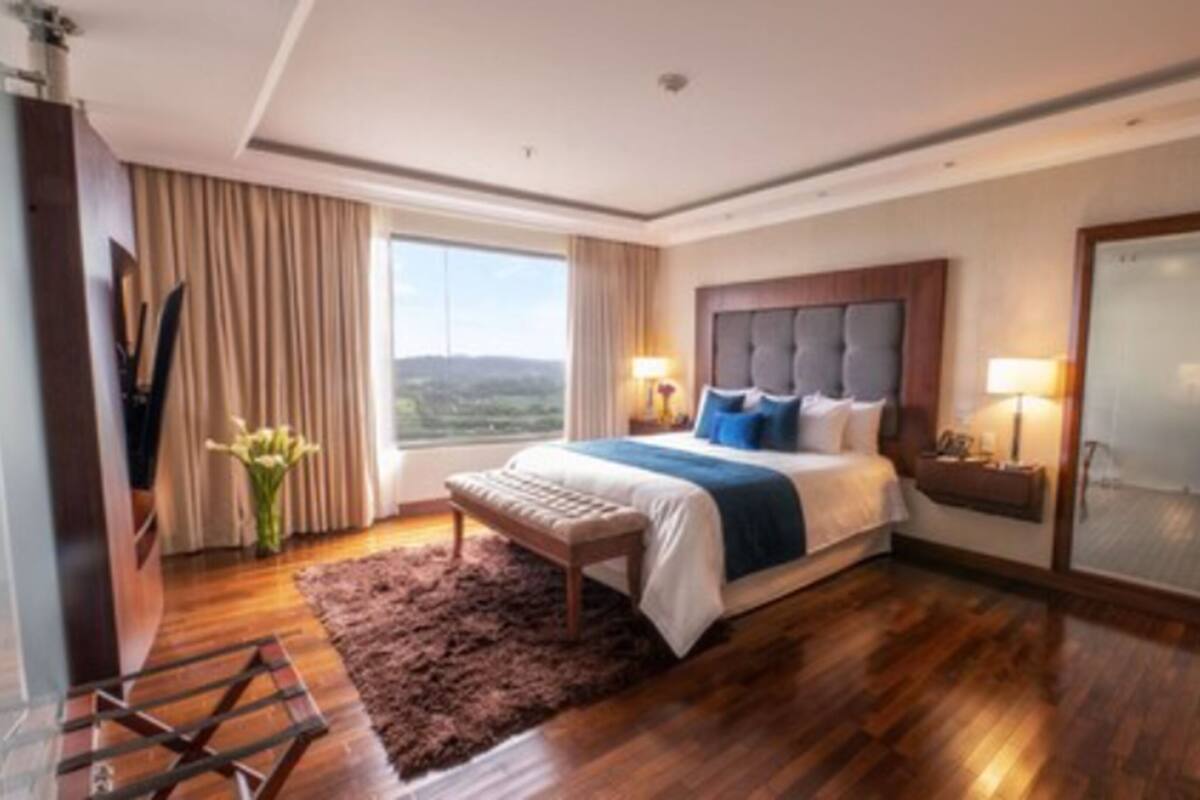 A hotel room with a large bed, a view of the outdoors, a wooden floor, and a mirror on one wall.