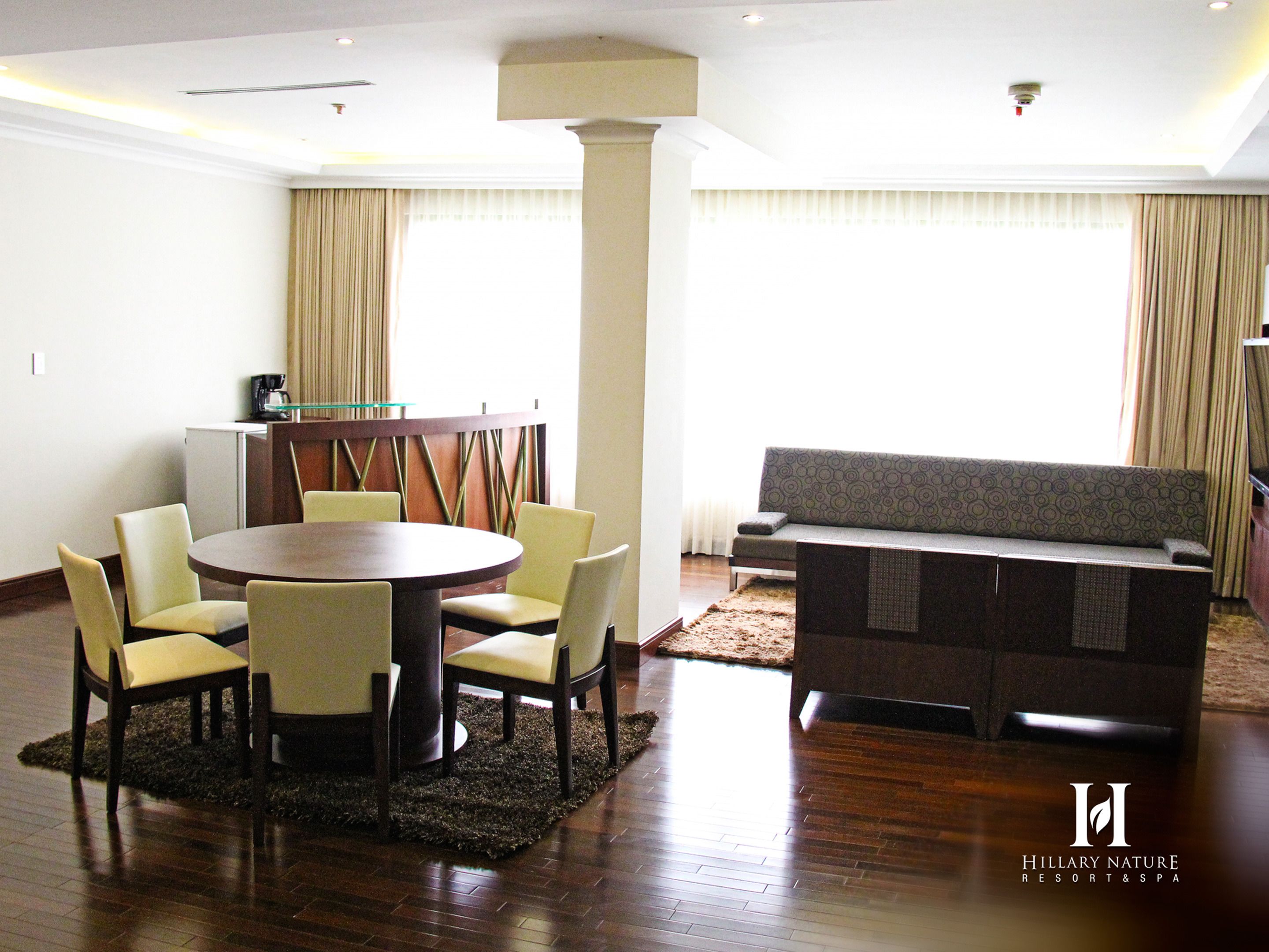 Una habitación de hotel moderna con una mesa redonda de comedor, cuatro sillas, un sofá y un televisor.