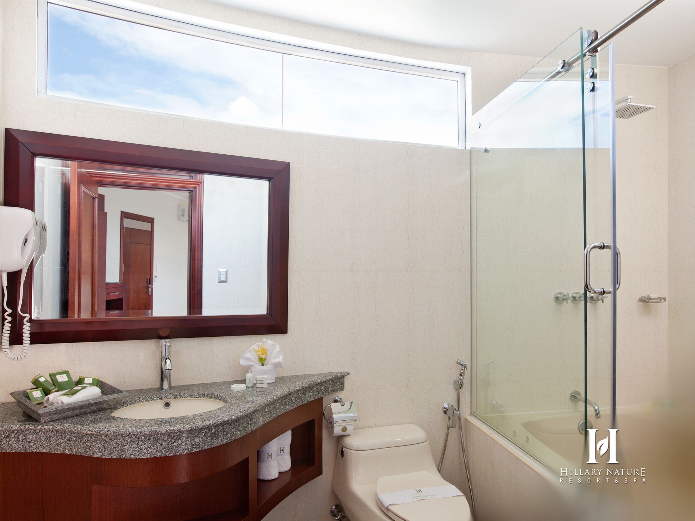 A modern bathroom with a granite countertop sink, a large mirror, a glass shower enclosure, and a toilet.