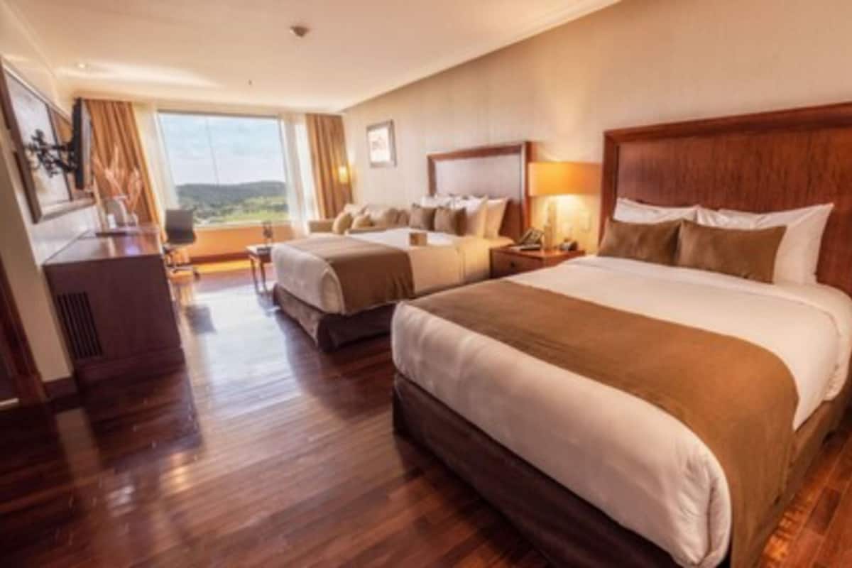 A hotel room with two beds, a desk, and a view of the outdoors.
