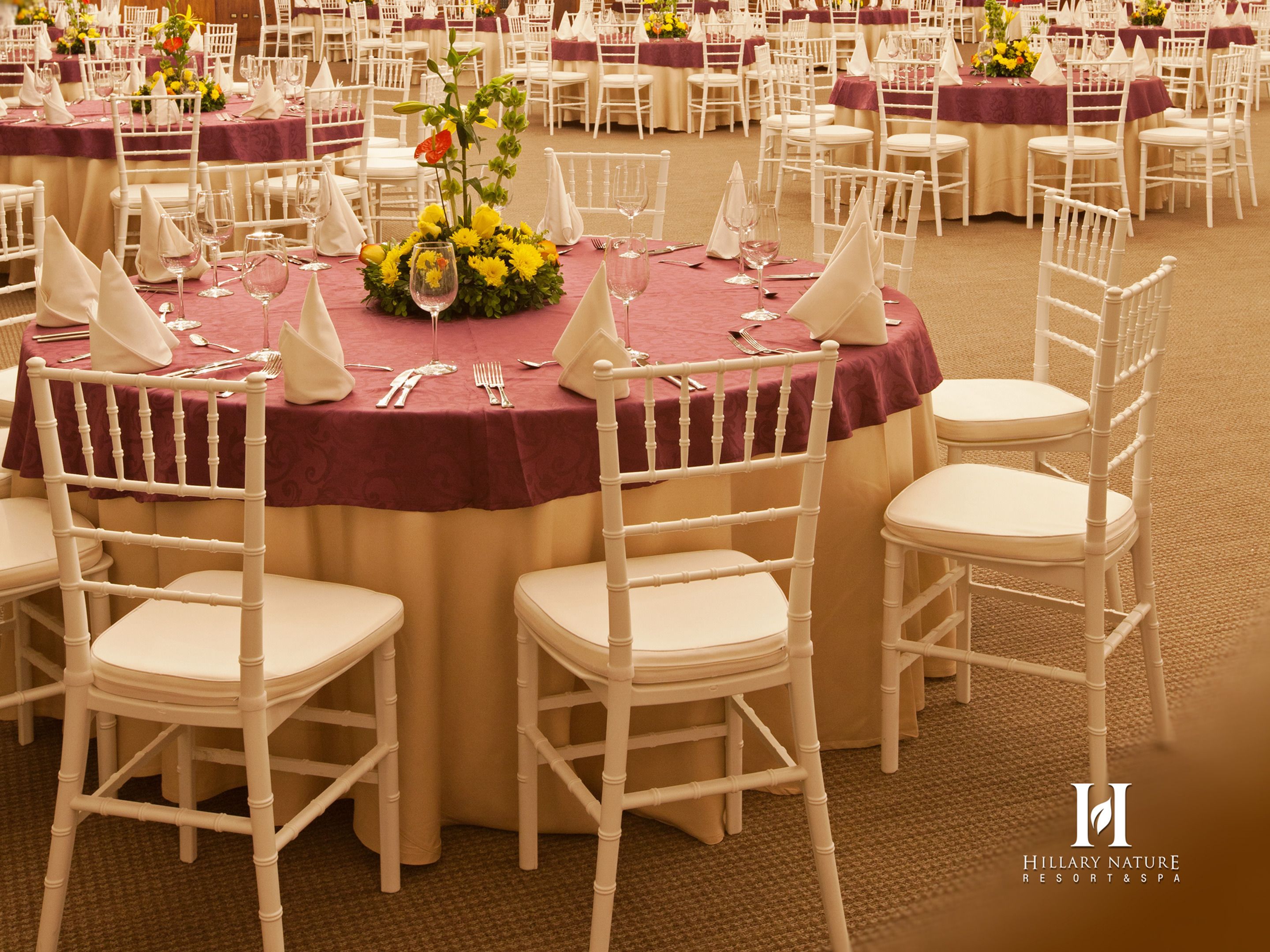 A banquet hall with round tables, white chairs, and red tablecloths.