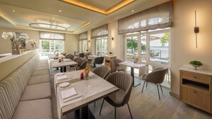 Un restaurante con una larga banqueta, varias mesas y grandes ventanales que ofrecen vistas al exterior.