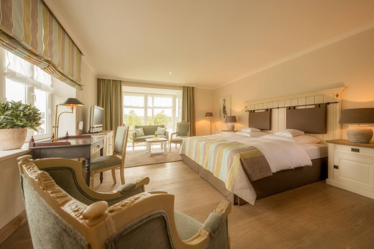 A hotel room with a bed, desk, chairs, a television, and a large window.