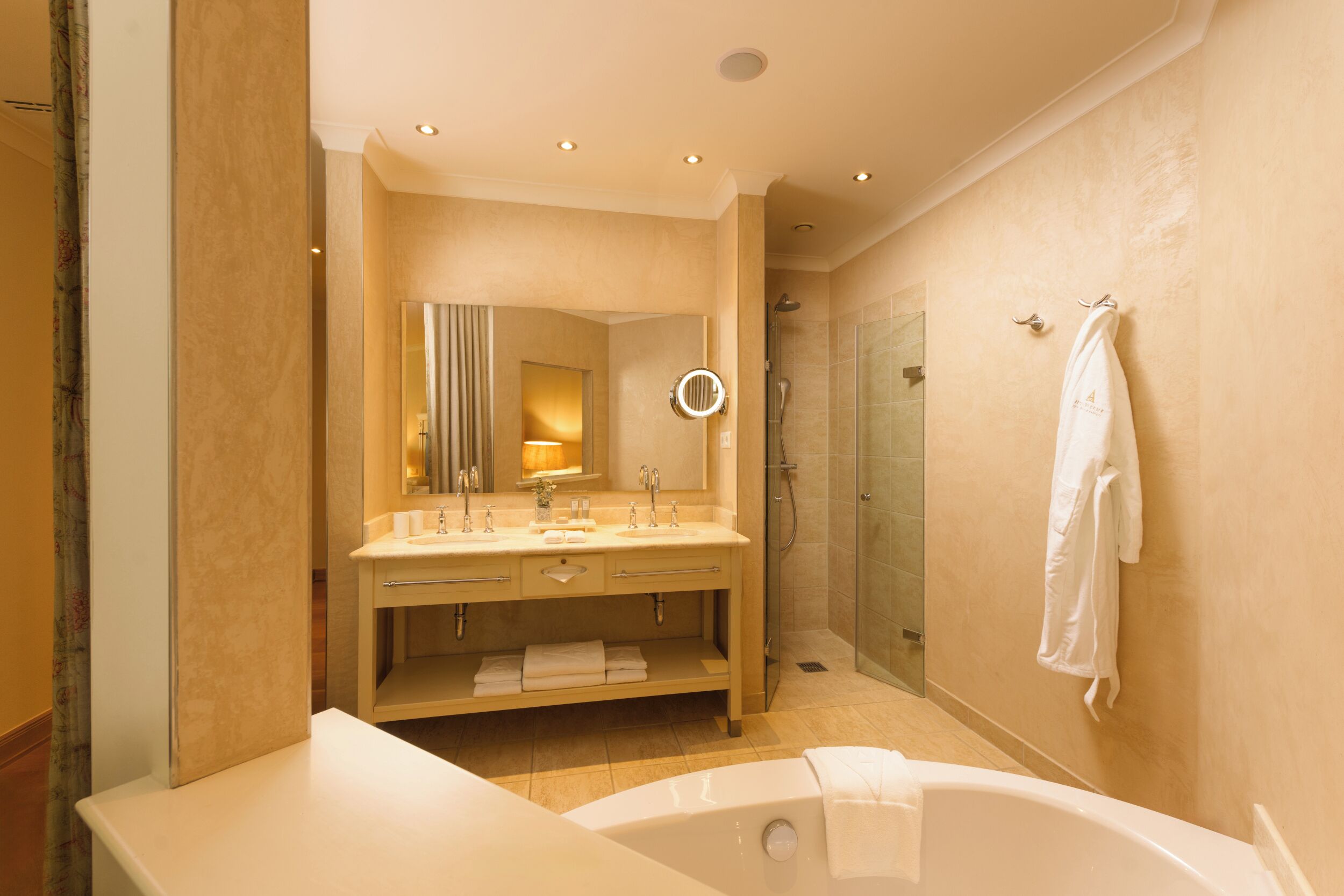 A modern bathroom with a bathtub, double sinks, a vanity with a mirror, and a shower area.