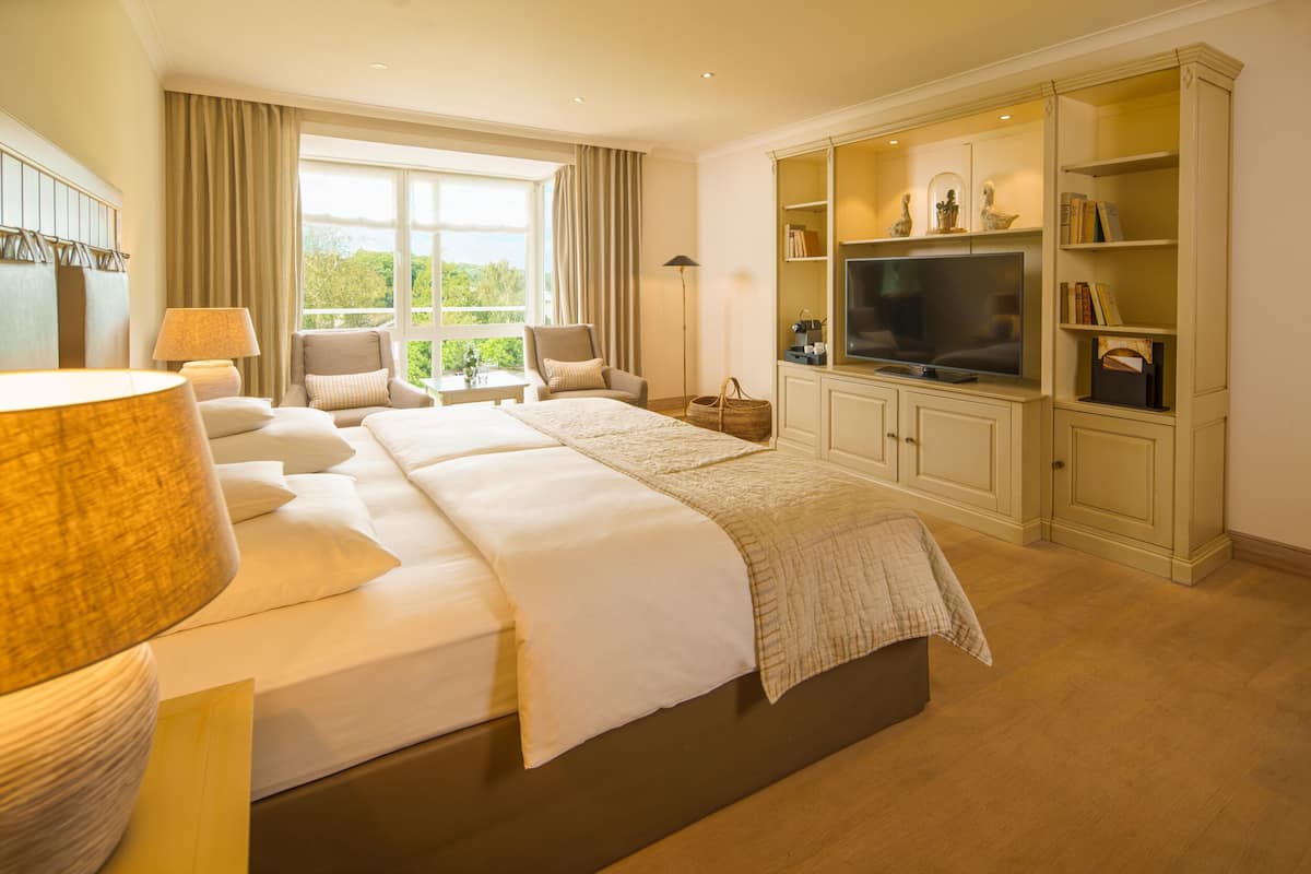 A hotel room with a large bed, a television, a bookshelf, and a window with curtains.