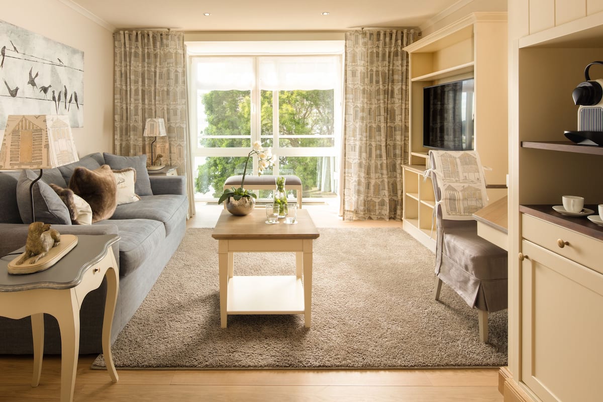 A living room with a grey sofa, a wooden coffee table, a TV on a stand, and a kitchen area with a kettle and cups.