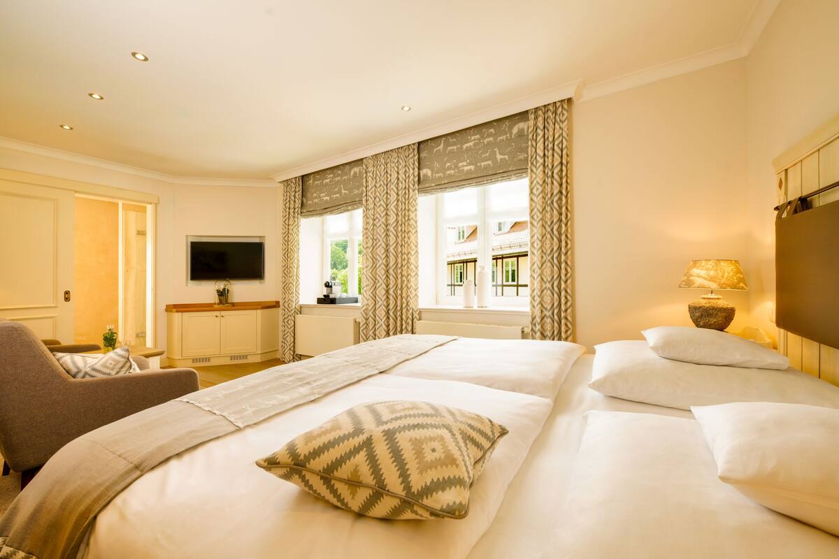 A hotel room with a large bed, a TV, a desk, and a window with curtains.