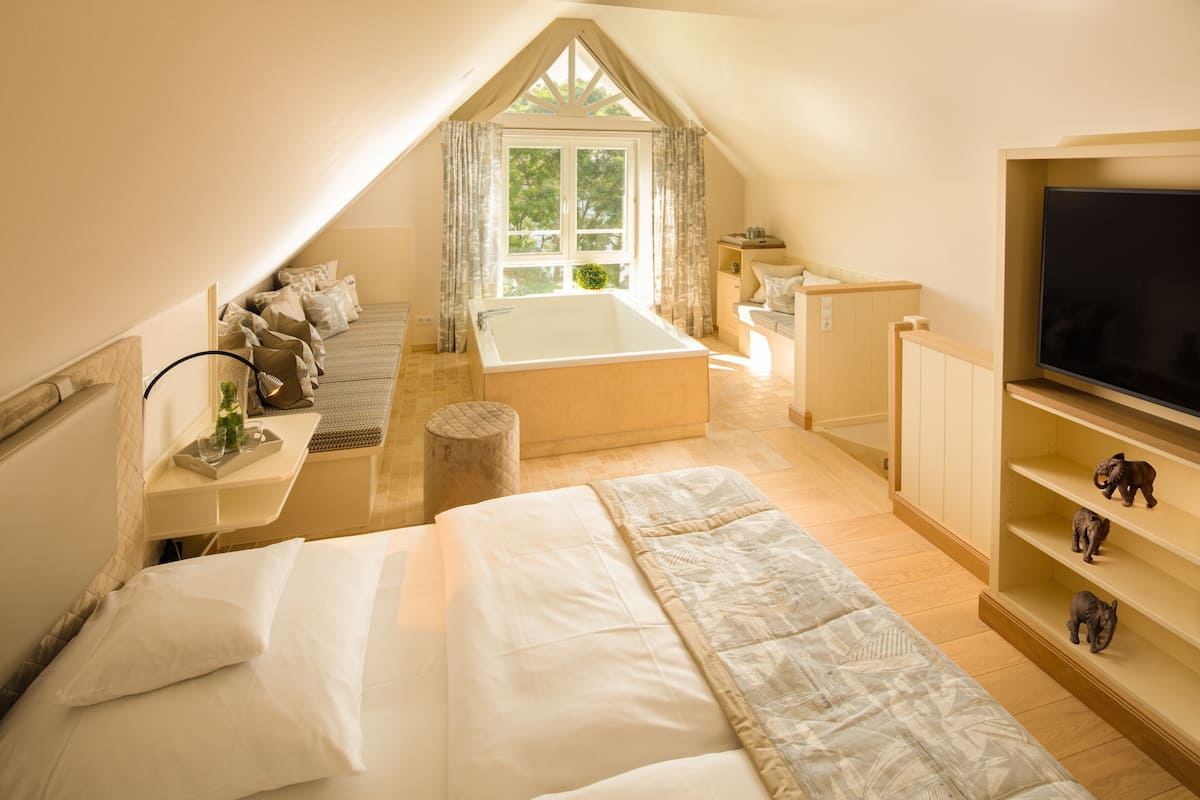 A bedroom with a bed, a bathtub, a TV, and a window with curtains.