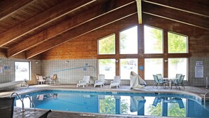 An indoor swimming pool with a wooden ceiling, large windows, and lounge chairs.