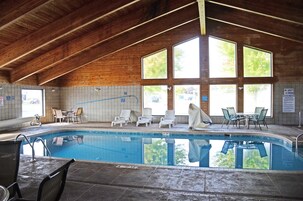 Piscina interna com teto de madeira, janelas amplas e espreguiçadeiras.