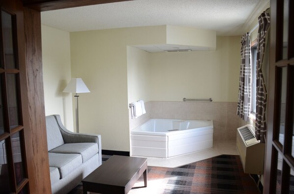 A room with a sofa, a small table, a bathtub, and a window with curtains.