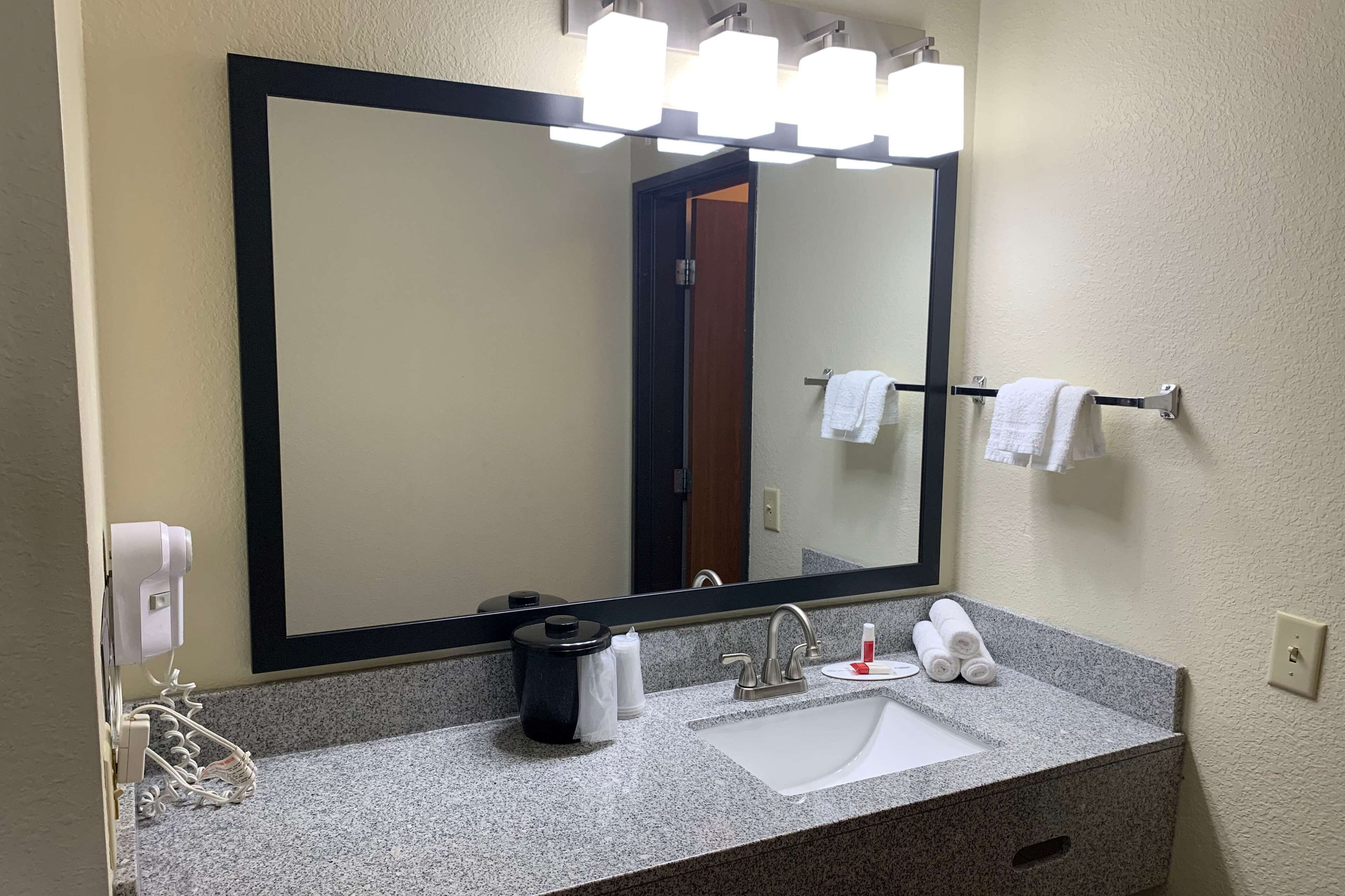 A bathroom with a large mirror, a sink, and a towel rack.