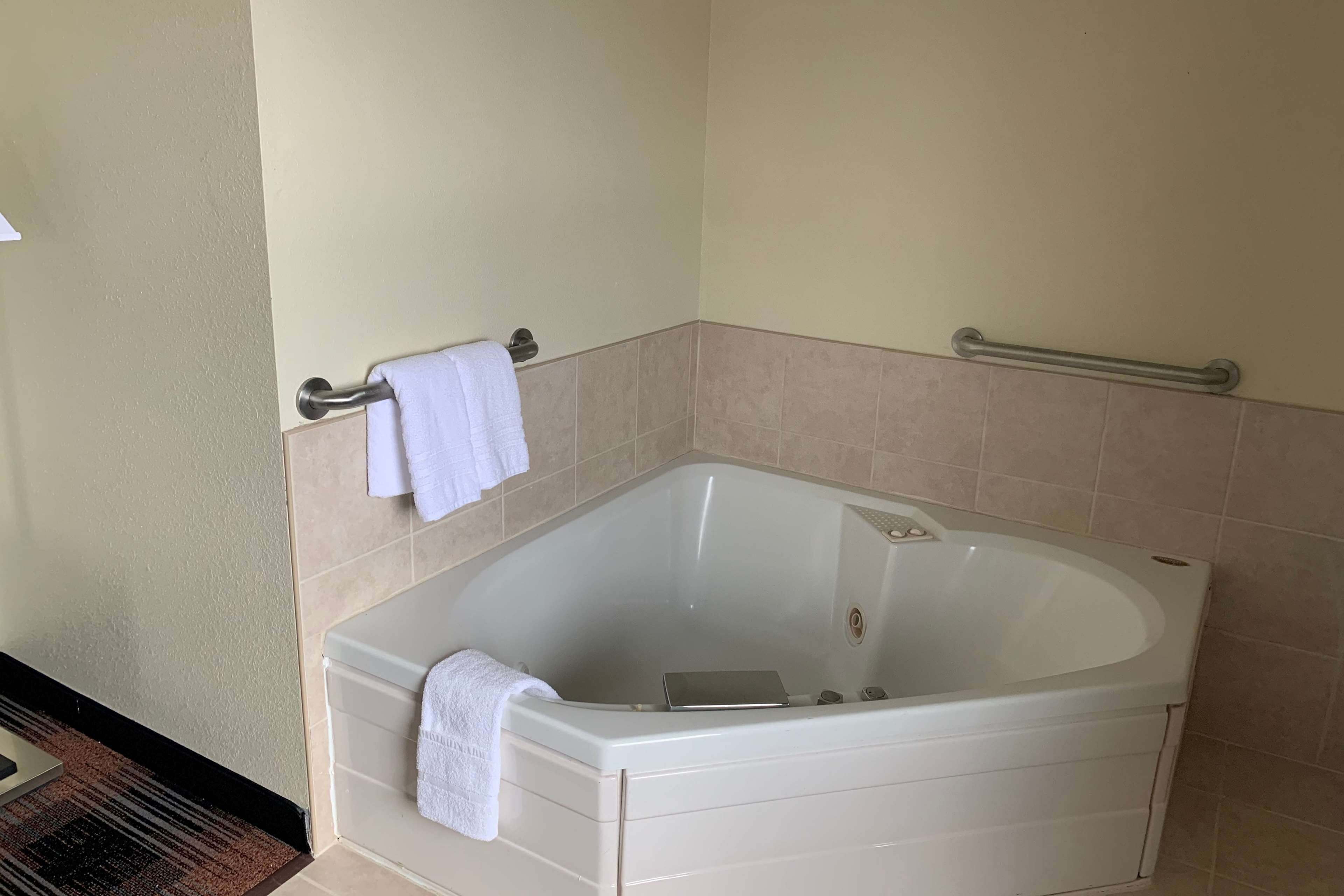 Un baño en esquina con una bañera blanca, un perchero y una barra de apoyo.