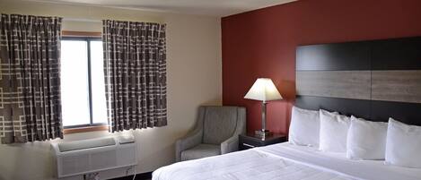 Habitación de hotel con una cama grande, una silla, un escritorio con lámpara y un aire acondicionado.