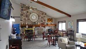 A spacious dining area with a stone wall and a large clock, wooden ceiling beams, and a variety of seating arrangements.