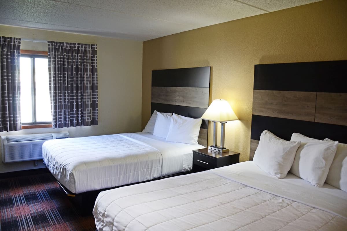 Une chambre d’hôtel avec deux lits, une table de chevet avec une lampe, une fenêtre avec des rideaux et un climatiseur fixé au mur.