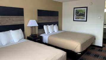 A hotel room with two beds, a nightstand with a lamp, a framed picture on the wall, and a carpeted floor.