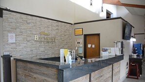 A reception desk at Baymont Inn & Suites with a stone wall backdrop, a wooden counter, and a mounted television.