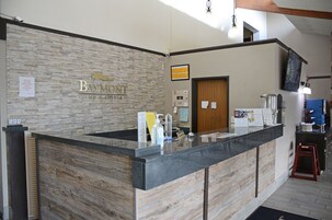Recepção do Baymont Inn & Suites com parede de pedra ao fundo, balcão de madeira e televisão na parede.