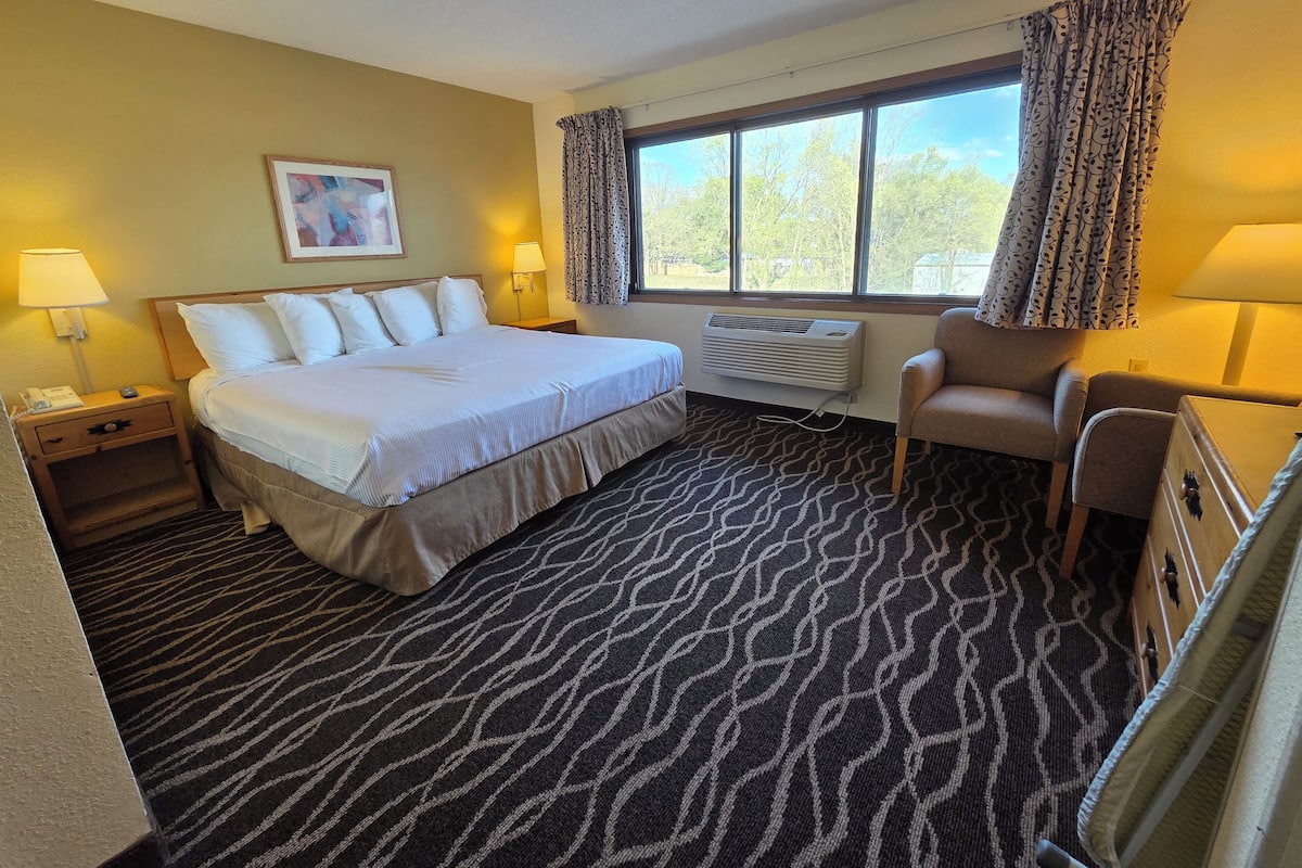Une chambre d’hôtel comprenant un lit, des lampes de chevet, une chaise, une fenêtre avec des rideaux et un climatiseur fixé au mur.