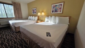Une chambre d’hôtel avec deux lits, une fenêtre avec des rideaux, un climatiseur fixé au mur, deux lampes de chevet et deux œuvres d’art encadrées.