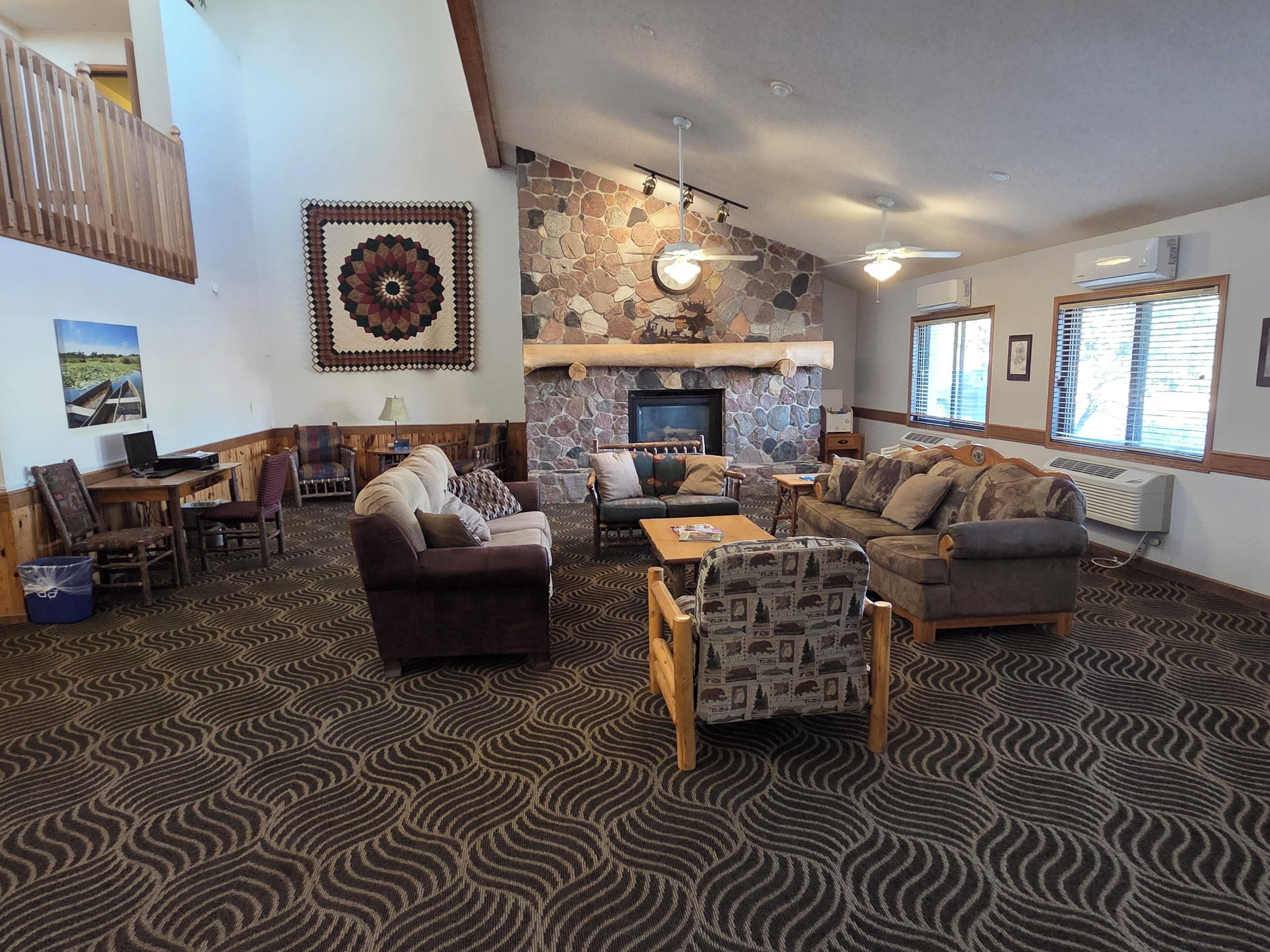 A spacious living area with a stone fireplace, multiple seating options, and a patterned carpet.