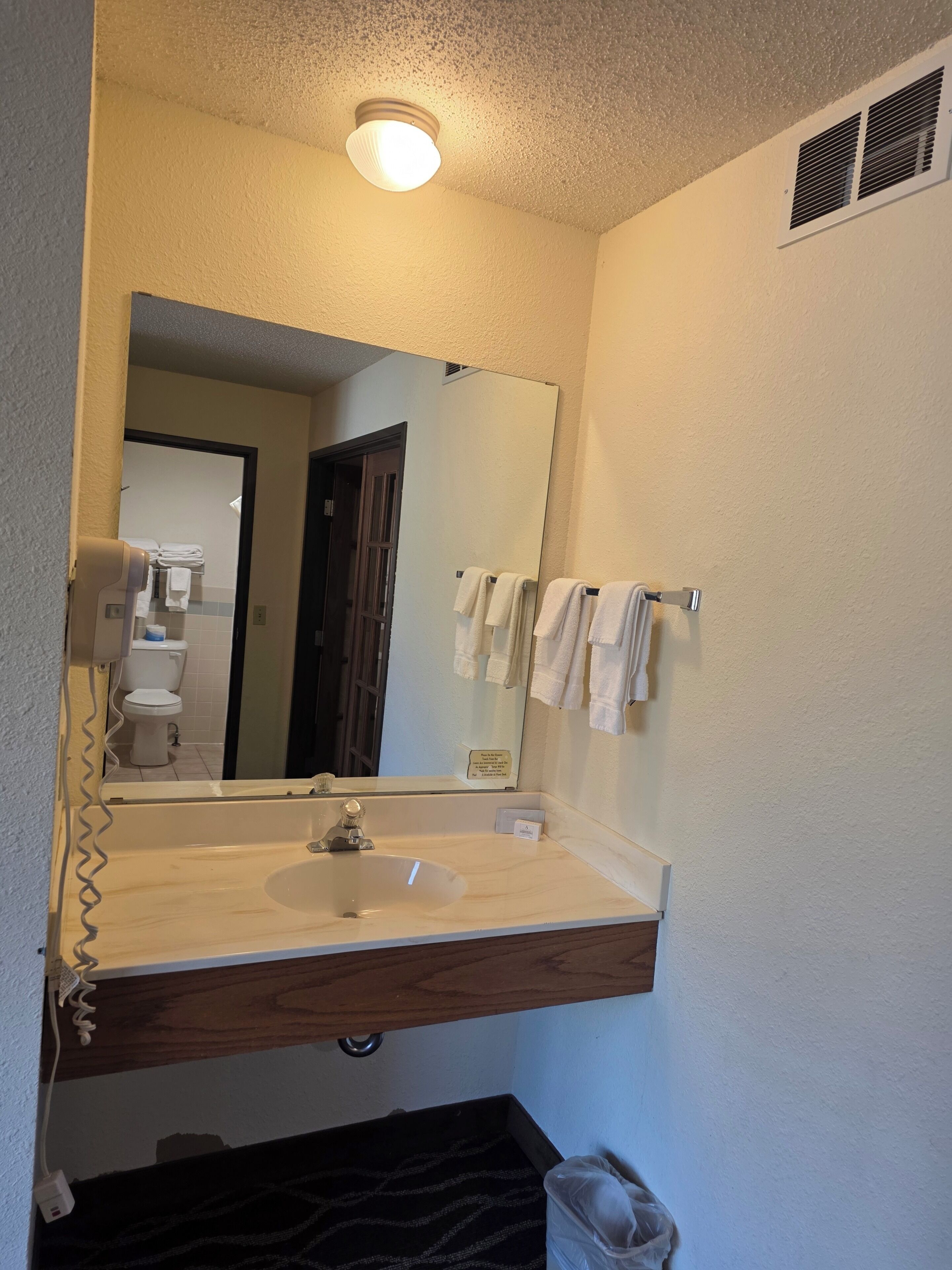 Un baño con un lavamanos blanco, un espejo, un perchero y una puerta visible que da a otra habitación.