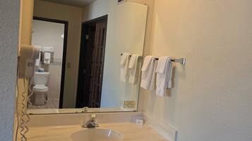Un baño con un lavamanos blanco, un espejo, un perchero y una puerta visible que da a otra habitación.