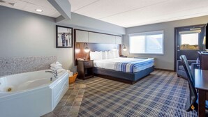 A hotel room with a large bed, a separate bathroom with a bathtub, a desk, and a chair. - AmericInn by Wyndham Madison South (Madison)