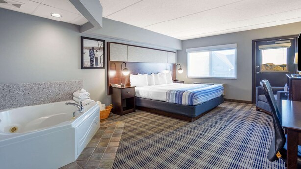 A hotel room with a large bed, a separate bathroom with a bathtub, a desk, and a chair. - AmericInn by Wyndham Madison South (Madison)